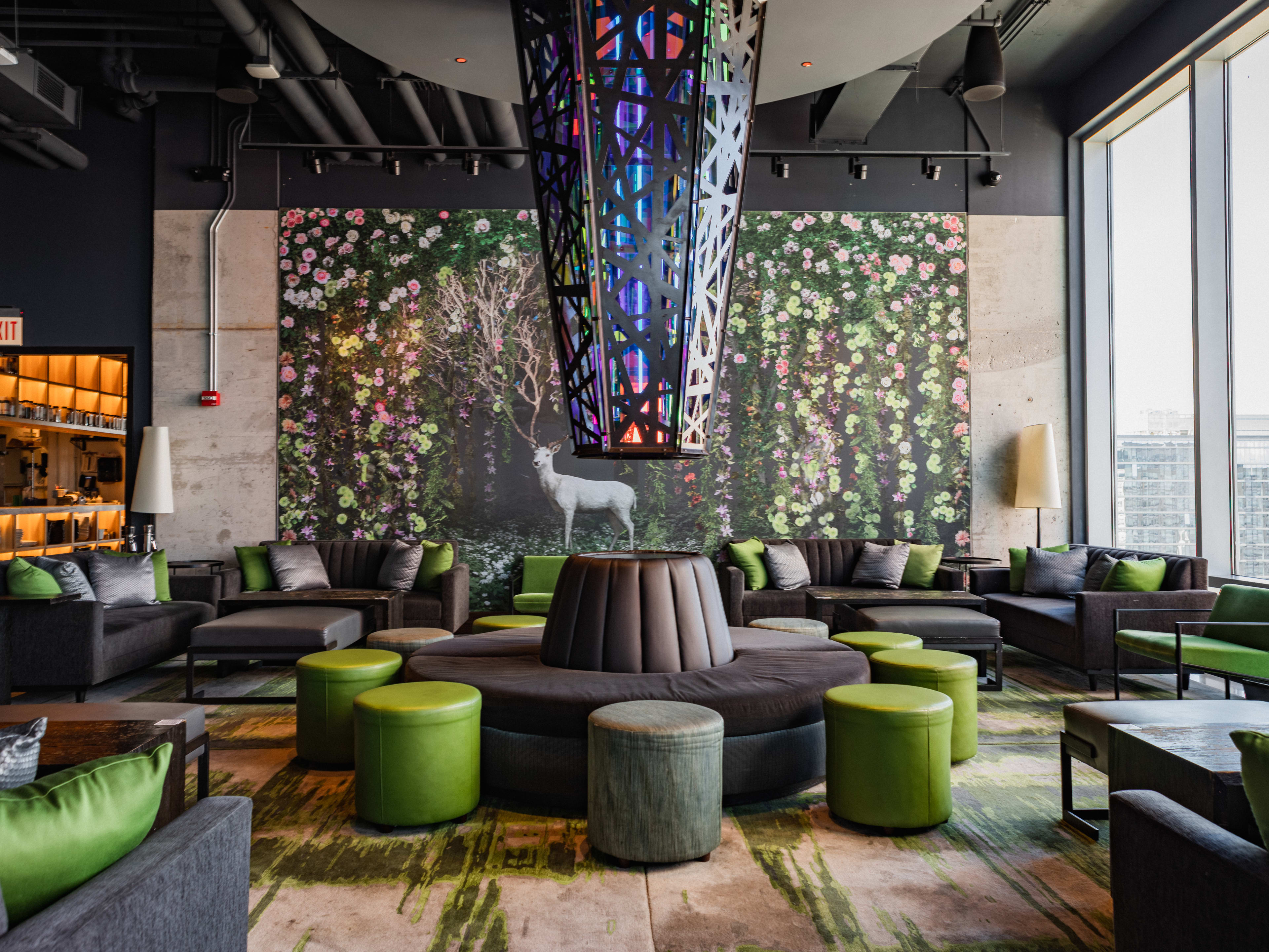 Lounge seating around a central banquette, with a floral mural, stag statue, and a colorful glass pendant light overhead